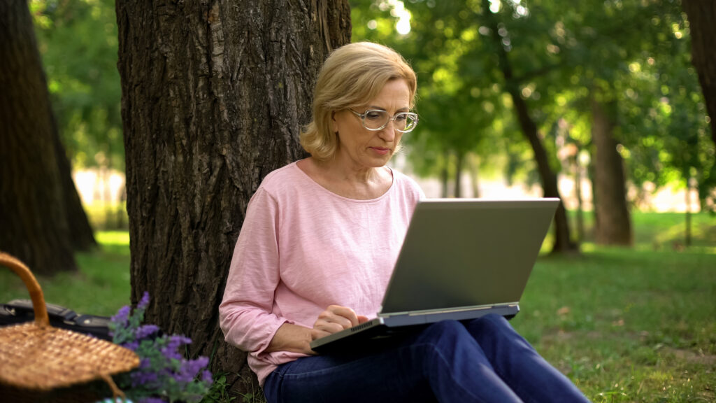 Senior woman sitting against a tree, surfing the web